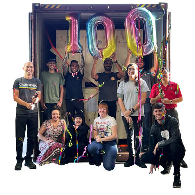 group of employees gathered in front of a loading dock filled with machines from the 100th shipment, with balloons overhead celebrating the milestone.